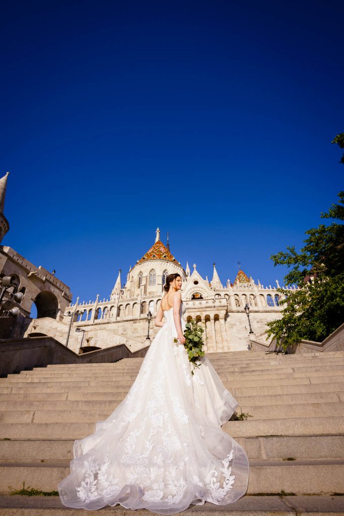 Elegáns, hajnali esküvői kreatív fotózás a Halászbástyánál Budapesten a Budai várban egy menyasszonnyal és egy vőlegénnyel.